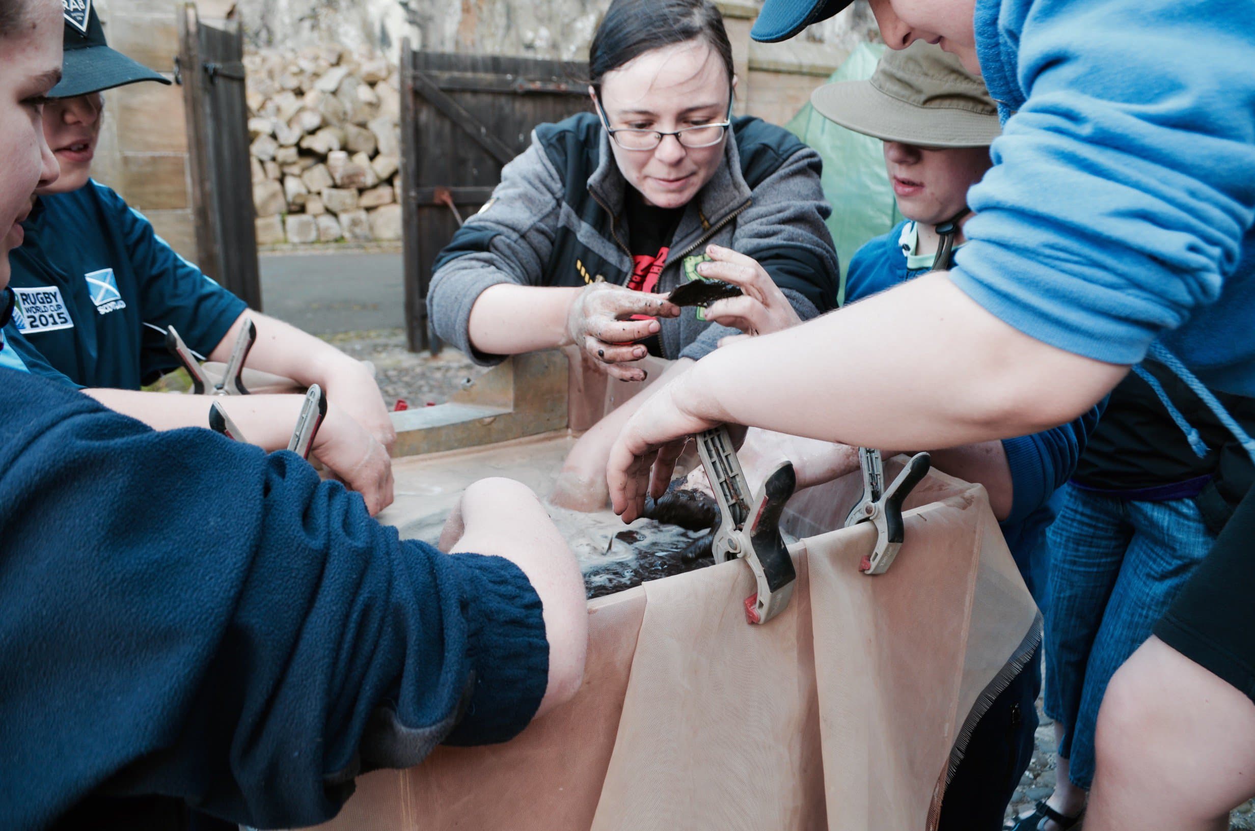 Two adults and three children stood around a flotation tank with their hands in water looking at something one of the adults is holding in her hand
