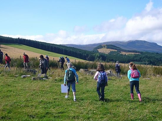 A group of children walking through a field, holding clipboards. Hills and fields can be see in the background.