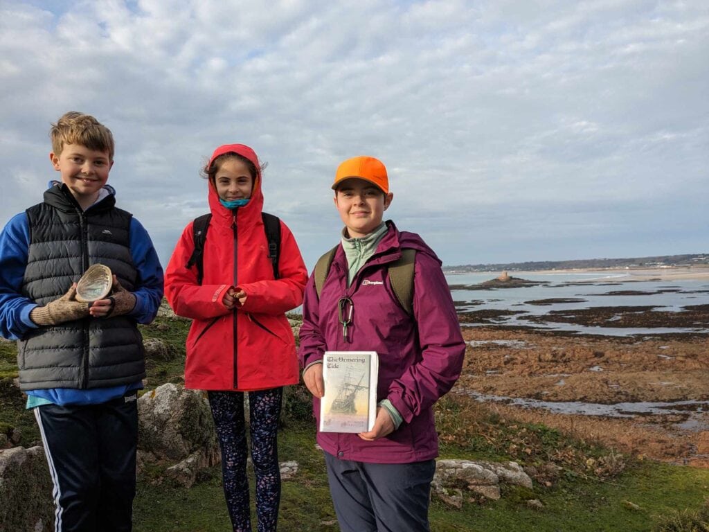 Three children standing on a windswept beach.