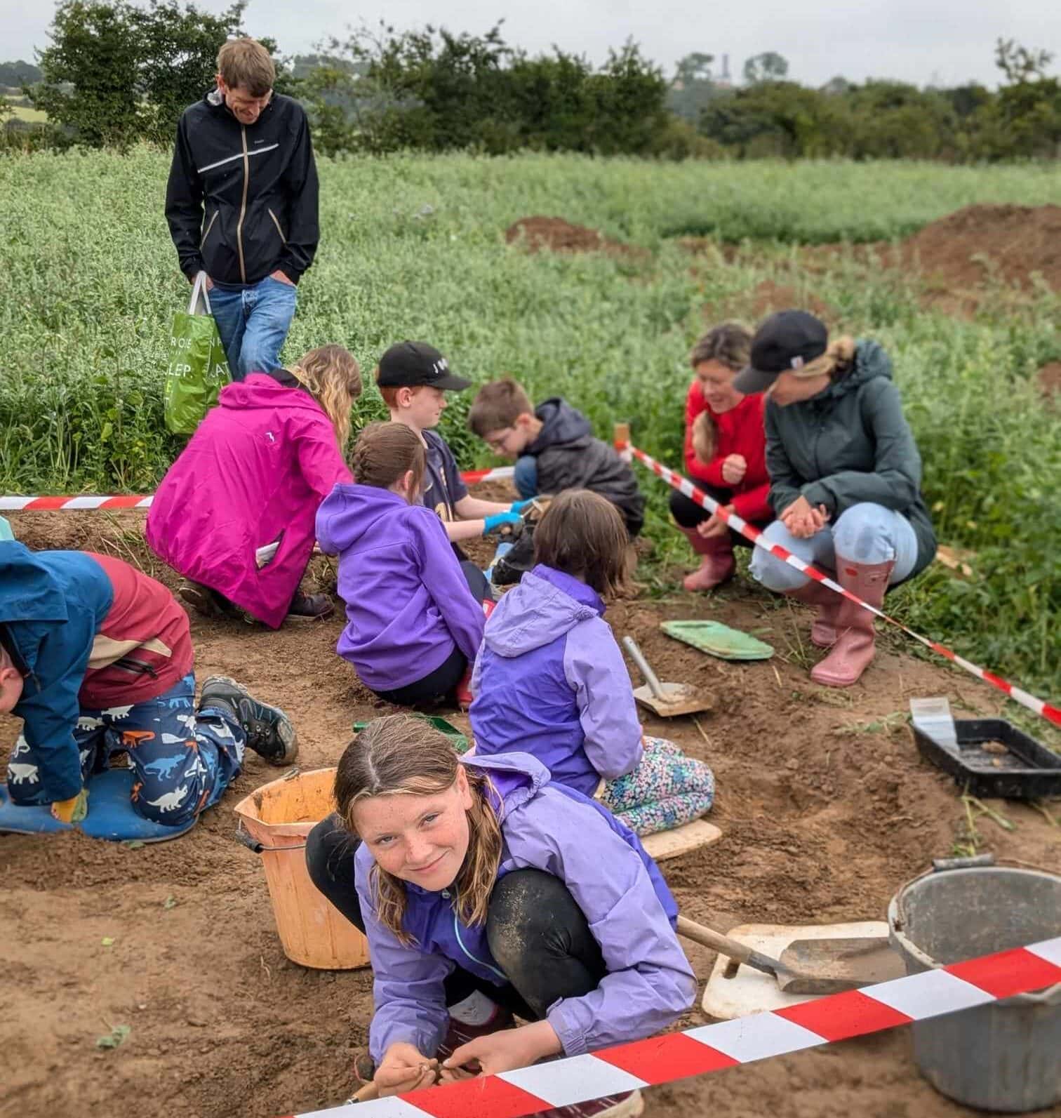 A group of 7 children and young people digging in an archeological excavation.