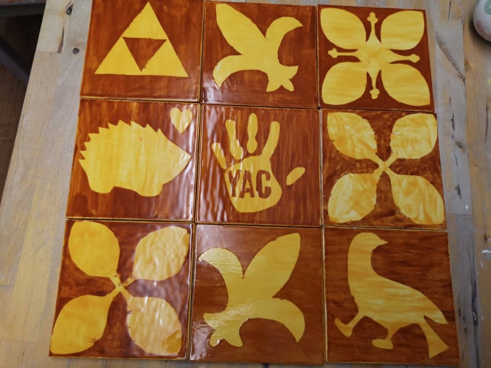 9 shiny brown and yellow square tiles, each with a different symbol. Some symbols are abstract shapes whereas some are animals such as a hedgehog and a bird.