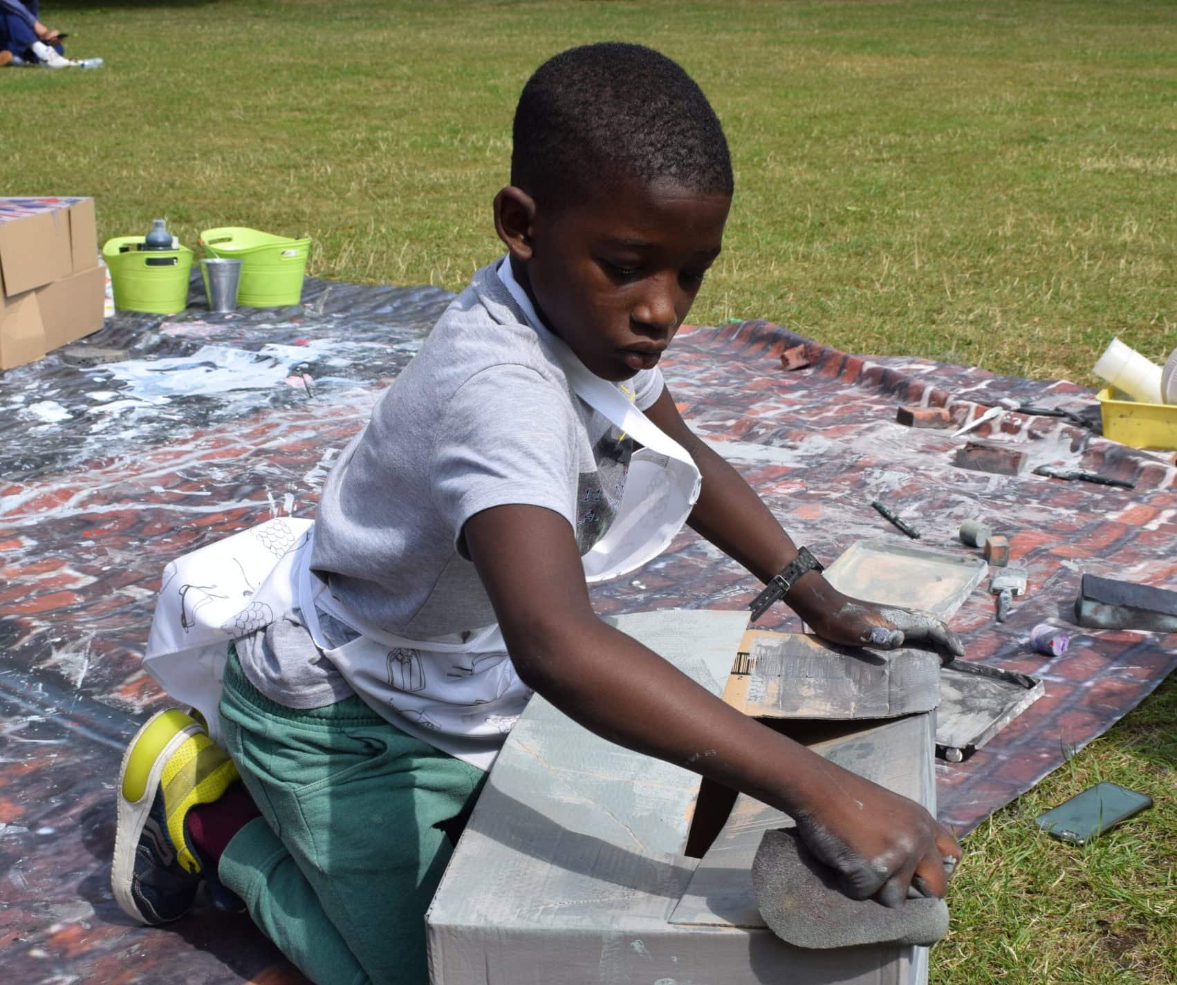 Young boy crafting with a large cardboard box in a grassy space