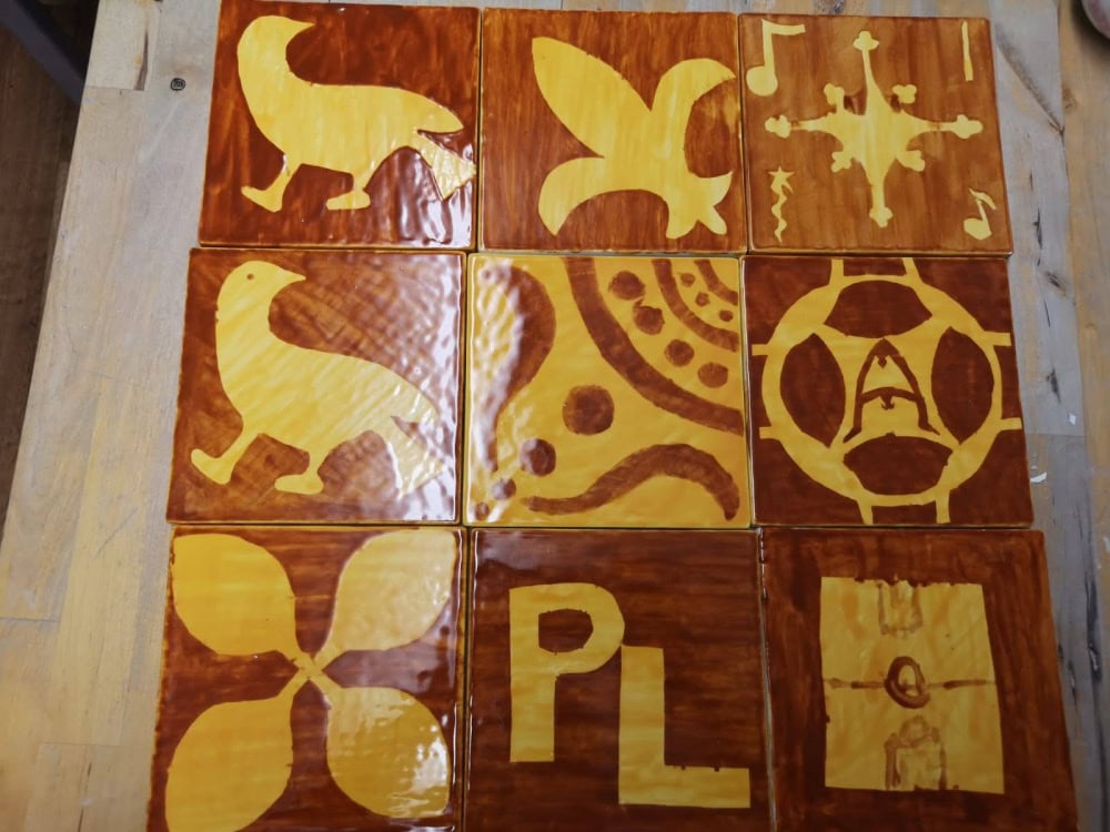 9 shiny brown and yellow square tiles, each with a different symbol. Some symbols are abstract shapes whereas some are bird shapes.