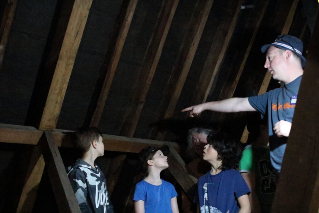 Four children and one adult stand in the attic of a historic building.