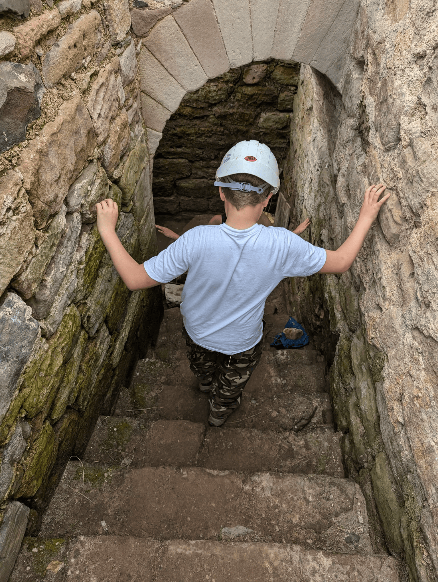 A child wearing a white hardhat descends a set of ancient stairs