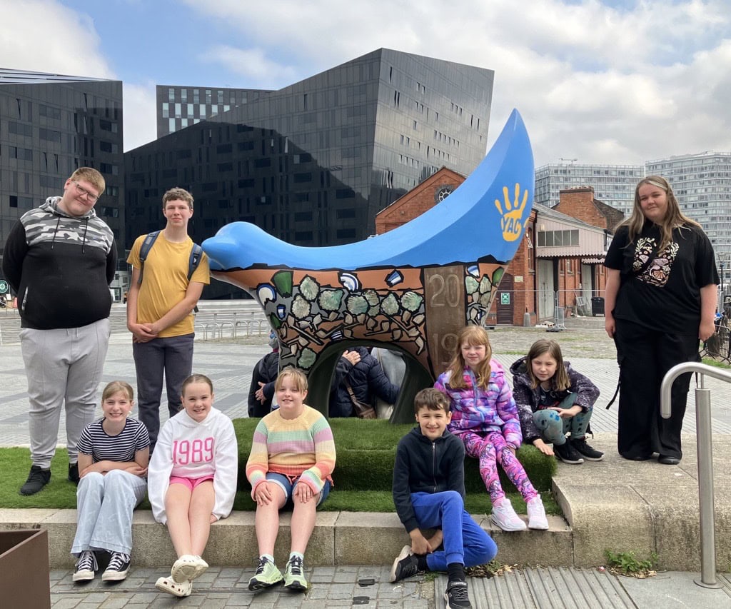Group of young people sat and stood in front of a SuperYAClambanana with ciuty scape in background