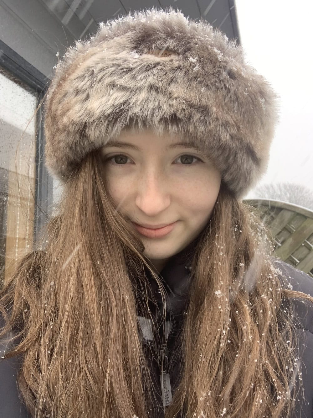 A selfie of a girl standing outside in the snow wearing a hat.