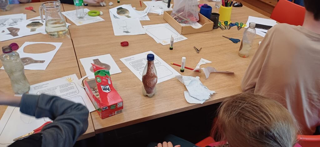 A table covering in paper, glue sticks, scissors, pens and pictures of historical bottles and jars.