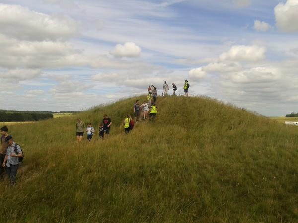 A group of adults and children climbing on top of a grassy barrow resembling a hill.