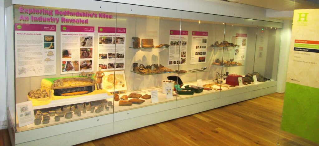 A display case in a museum containing ceramic artefacts and a replica kiln made from cardboard and clay.