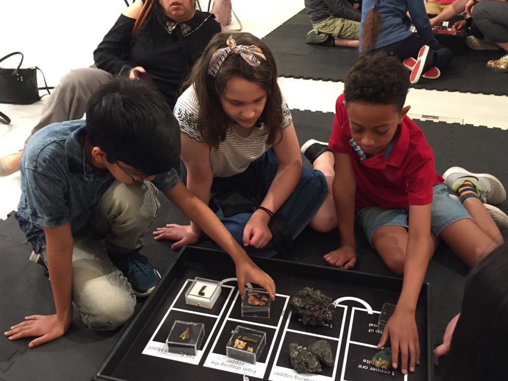 Three young people sat on the floor looking at artefacts in boxes.