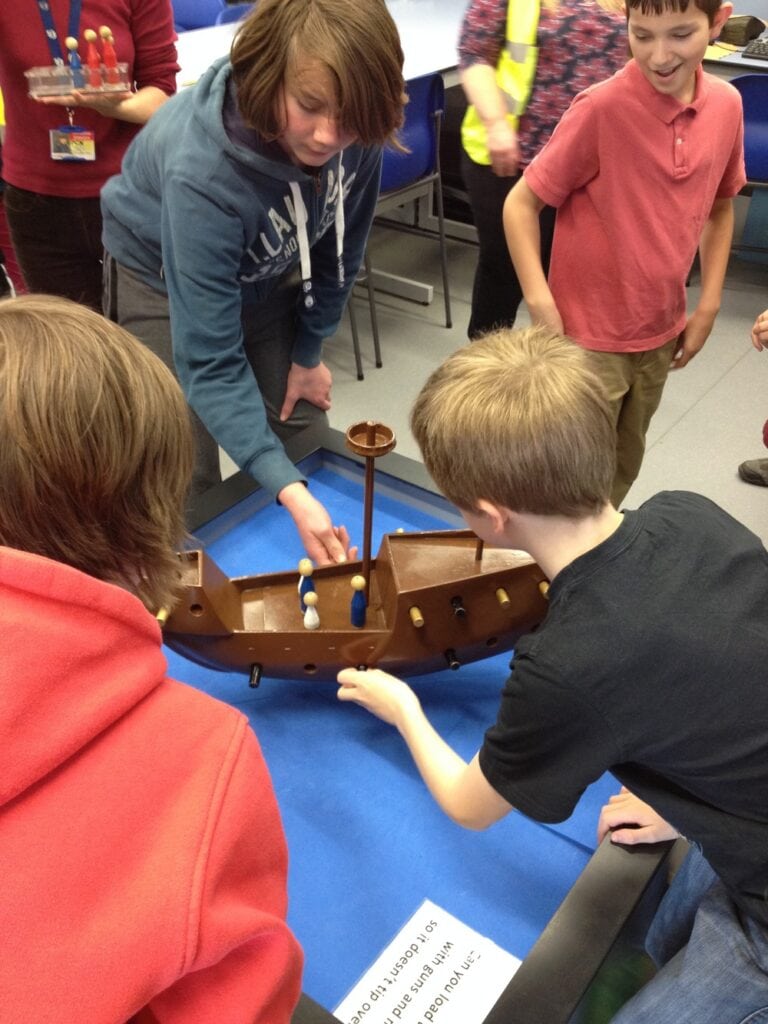 Four children gather around a wooden model of an early modern ship.