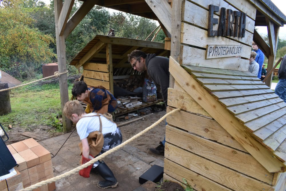 Two young people and one adult crouch in a wooden structure outside.