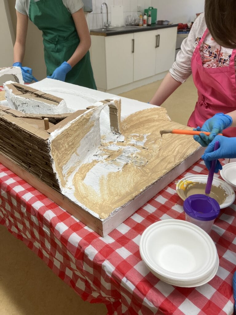 Young people painting a structure made from cardboard