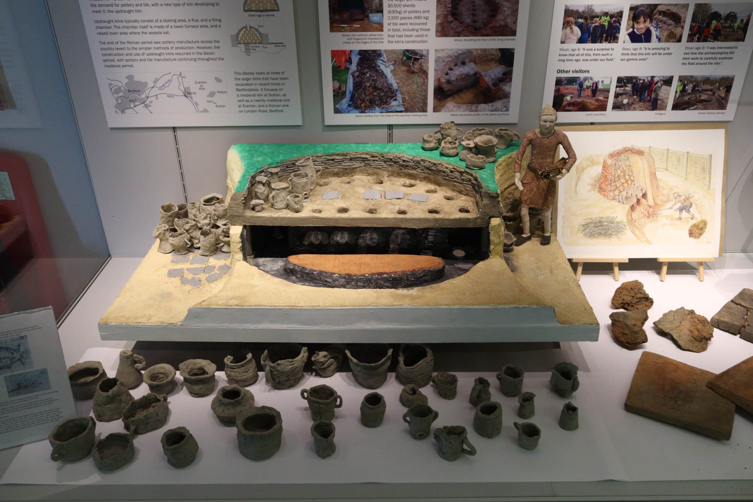 A table-top display of a replica post-medieval kiln, a doll figure of a potter and lots of small replica pots.