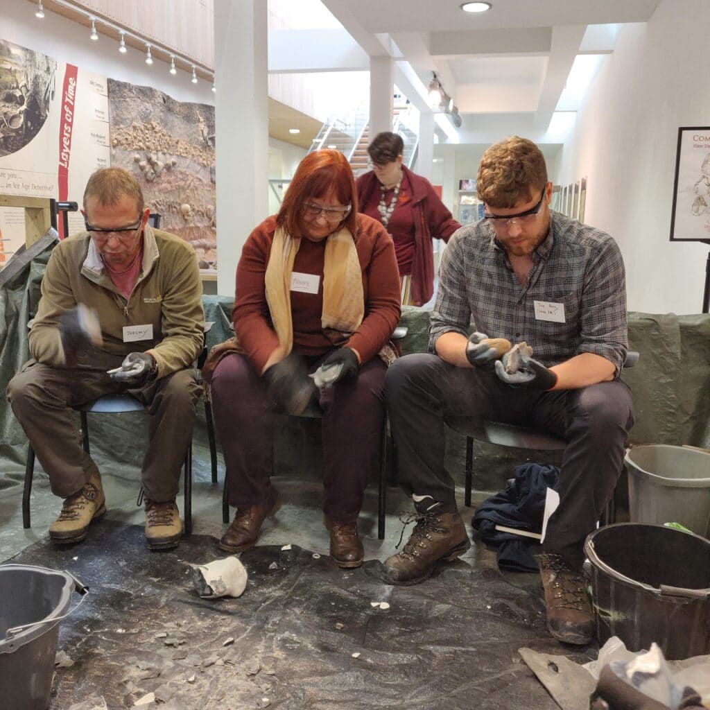 Three people sat wearing safety goggles knapping fliny