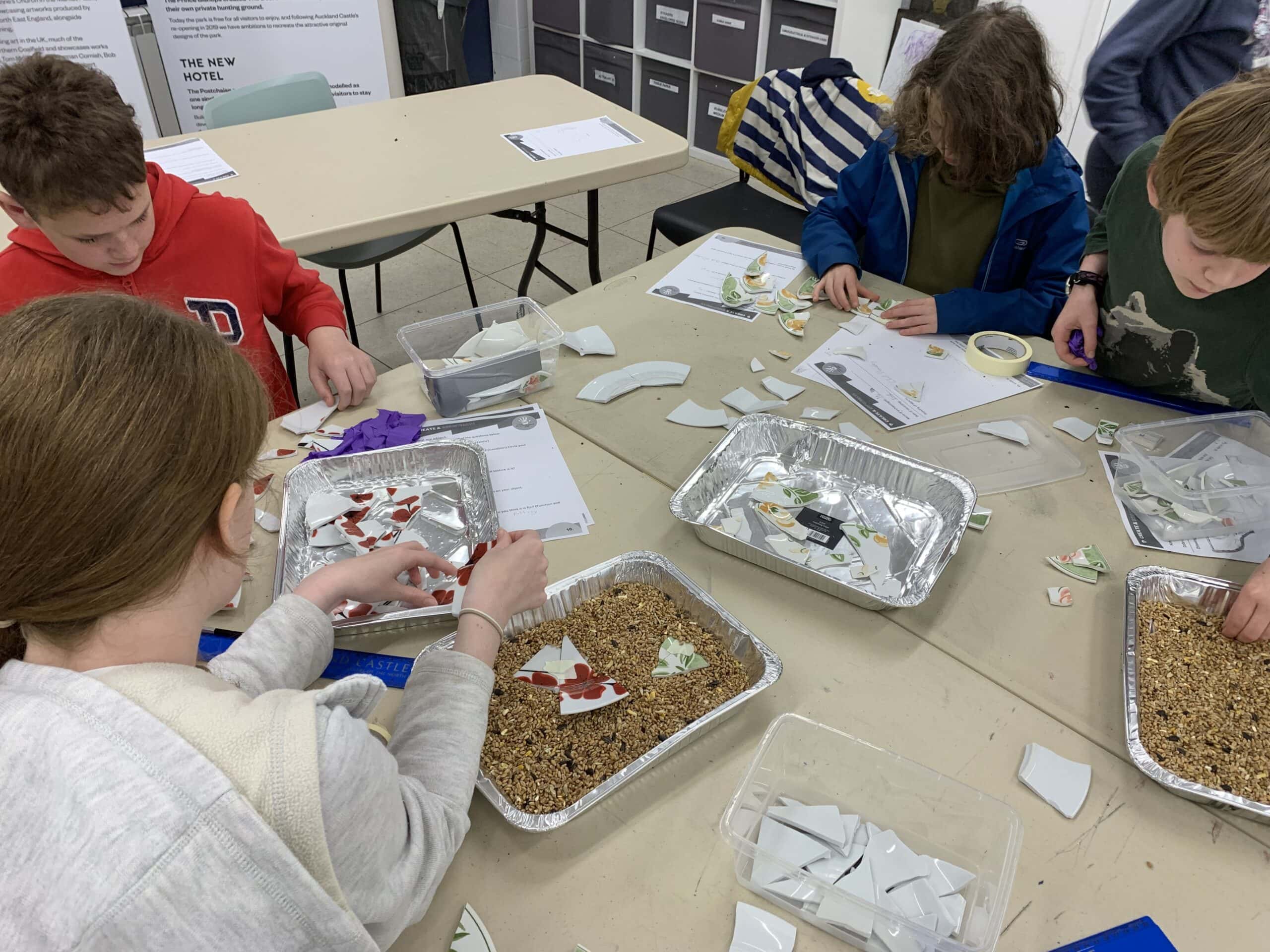 A group of young people sat at a table with foil trays filled with pottery sherds.
