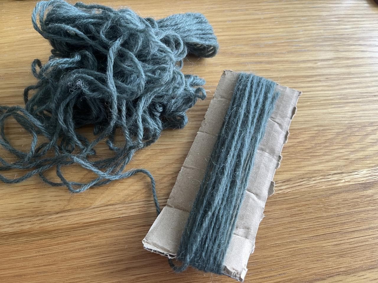Grey yarn partly wrapped around a strip of cardboard.