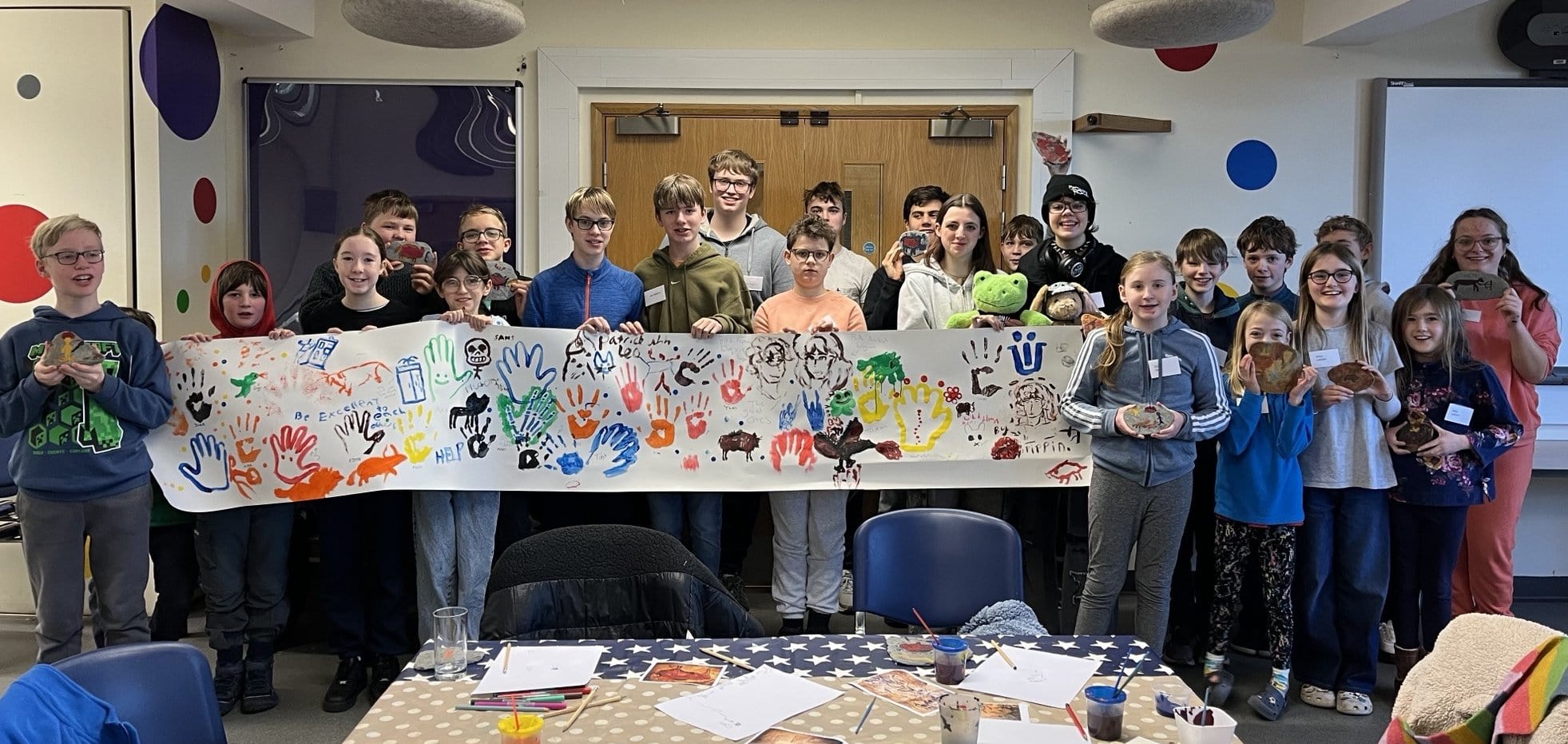 Image of children and young people stood in a line behind a long piece of paper with cave art decoration.