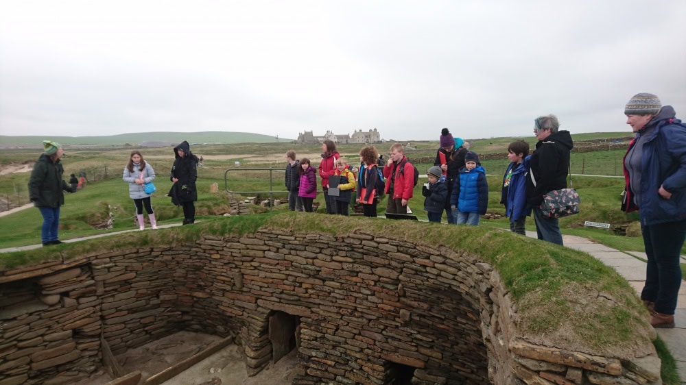 A group of adults and young people standing around edge of ancient stone buildings.