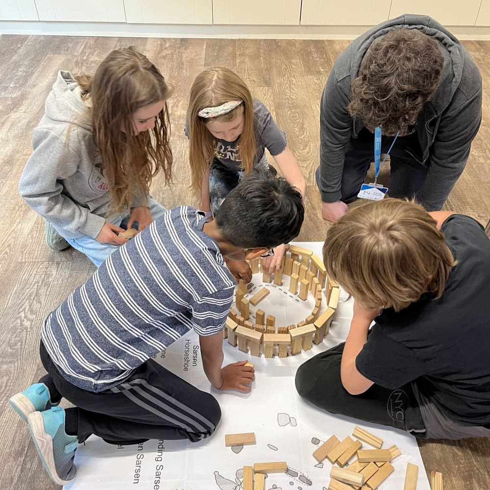 Five children building a model of Stone Henge out of small wooden blocks.
