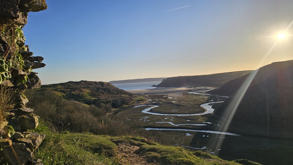 A coastal landscape with a river leading to the beach and grassy fields.