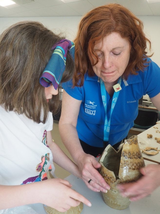An adult showing a young person some pieces of pottery.