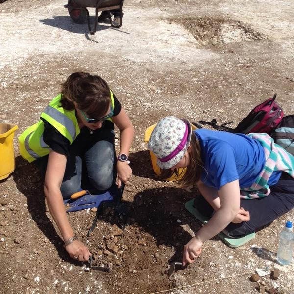 An adult and a child excavate using trowels on an archaeological dig.