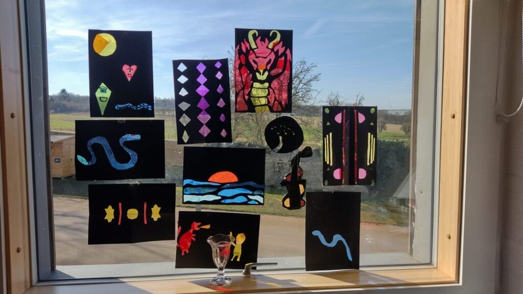 Crafted pictures in the style of stained glass windows displayed on the window of a building.