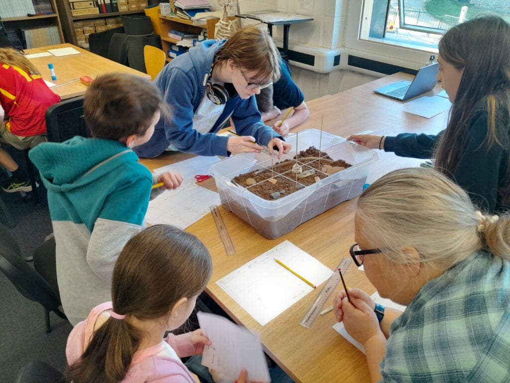 Children sat around a table with a box of sand and artefacts.
