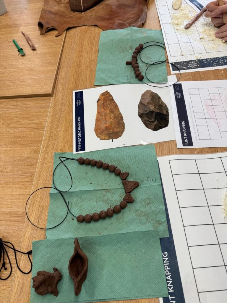 Strings of beads made from clay and printed photographs of stone age tools on a table.
