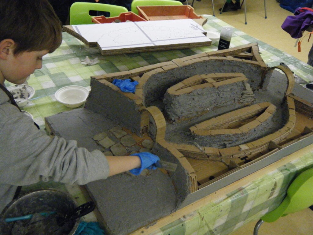 Young people adding clay to a model kiln on top of a table