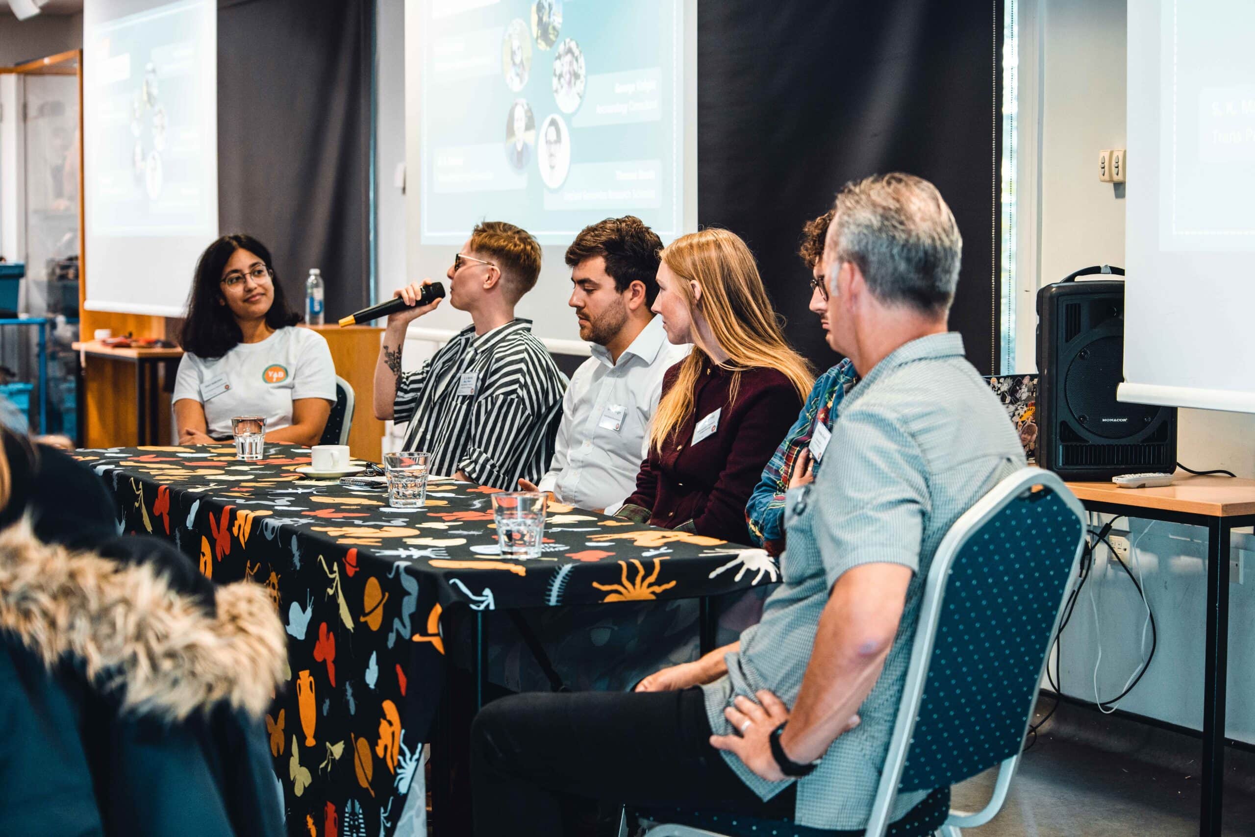 Group of adults sat at a table answering questions using a microphone