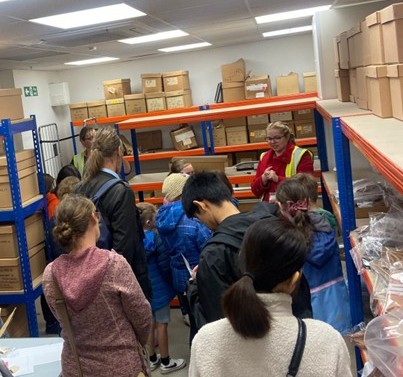 A group of young people in a modern museum archive, standing in a room lined with shelves of boxes.