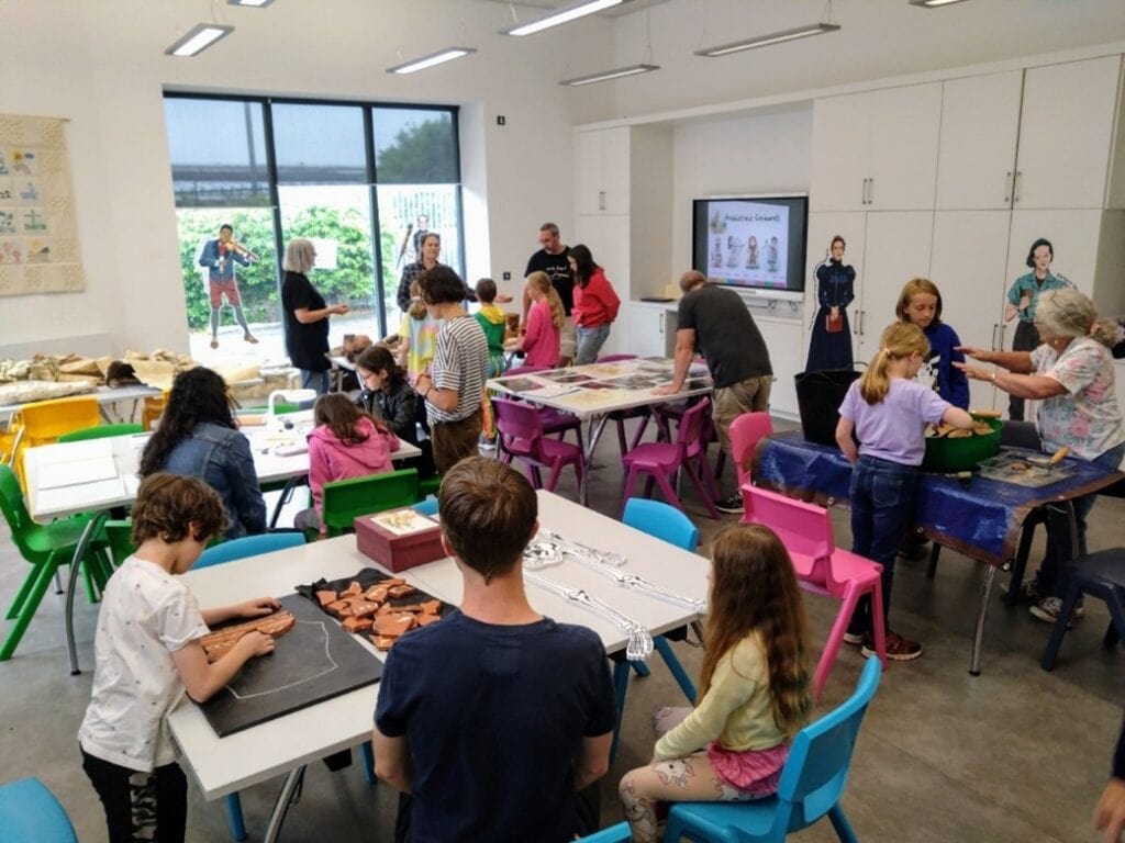 Young people and adults in a classroom, taking part in different activities on tables.