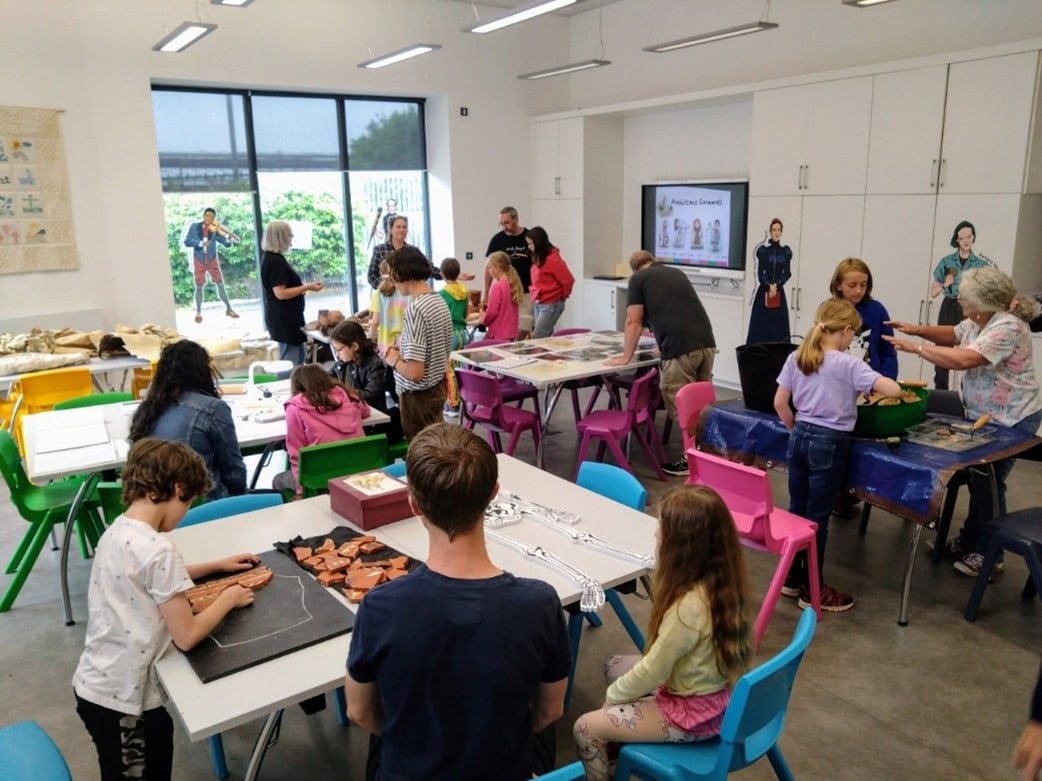 Young people and adults in a classroom, taking part in different activities on tables.