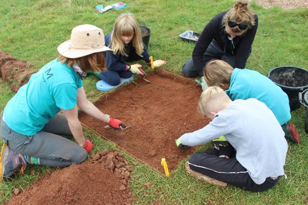 A group of young people excavating in a small square archaeological trench.