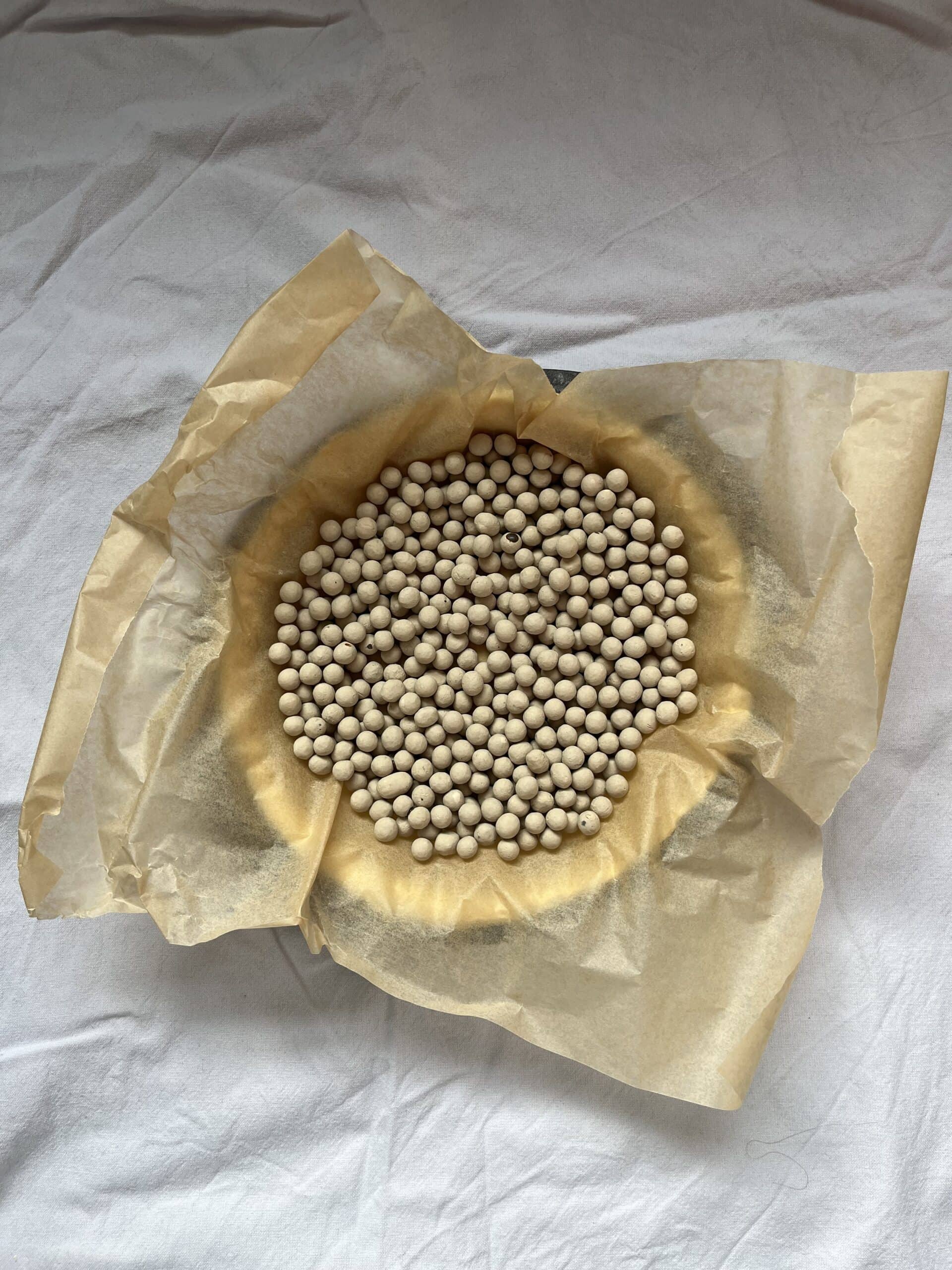 An uncooked pastry case in a metal tin, covered with a piece of brown grease-proof paper and clay baking beans.