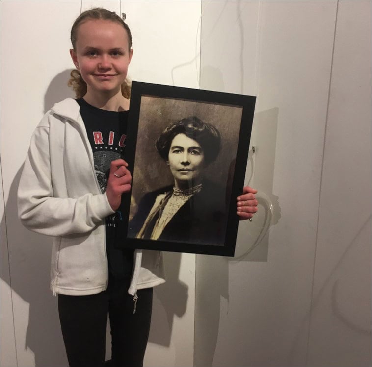A girl in a grey hoodie holds an old framed picture of a Victorian lady.