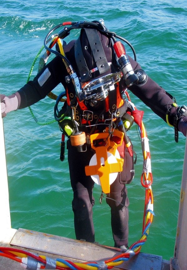 Image of diver stood on side of boat with sea in background.