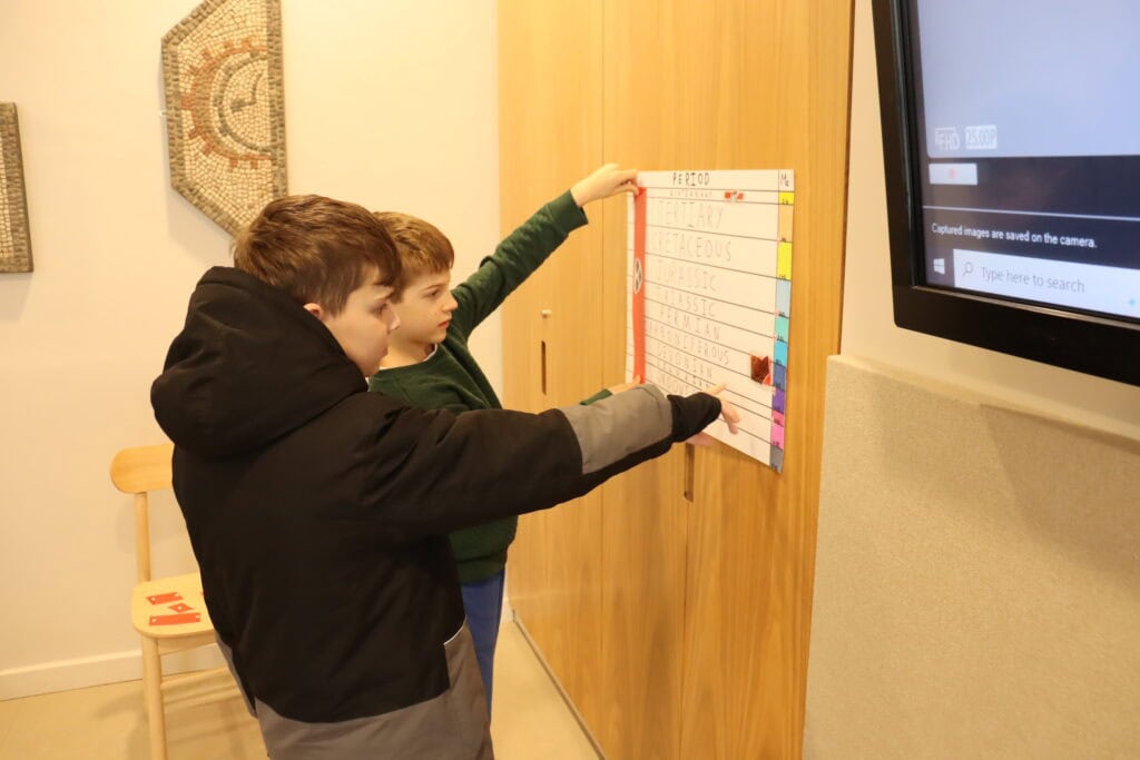 Two young people looking at a chart of geological periods on a wooden wall
