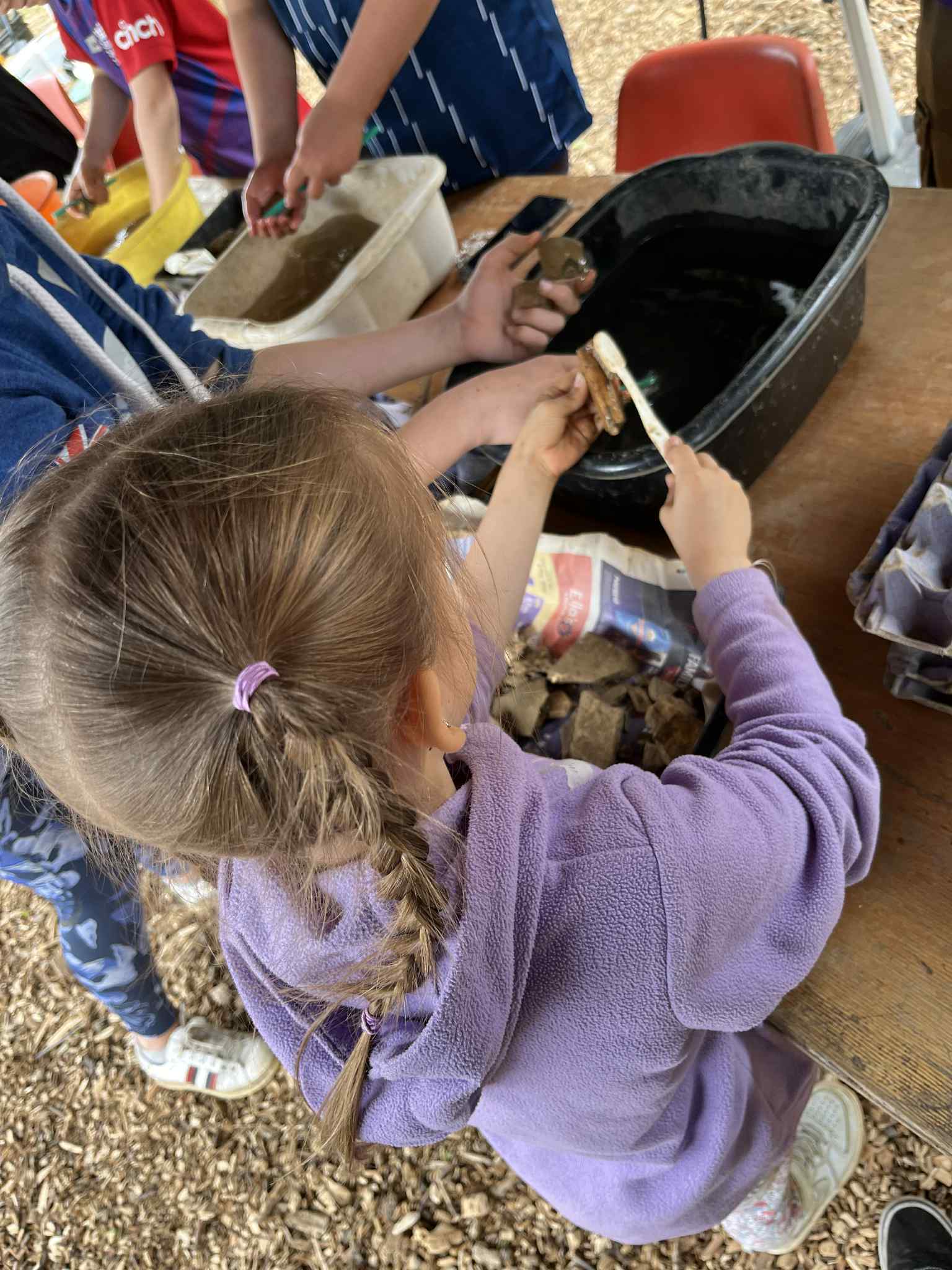 Child with pigtails wearing purple top. Holds toothbrush to clean animal bone