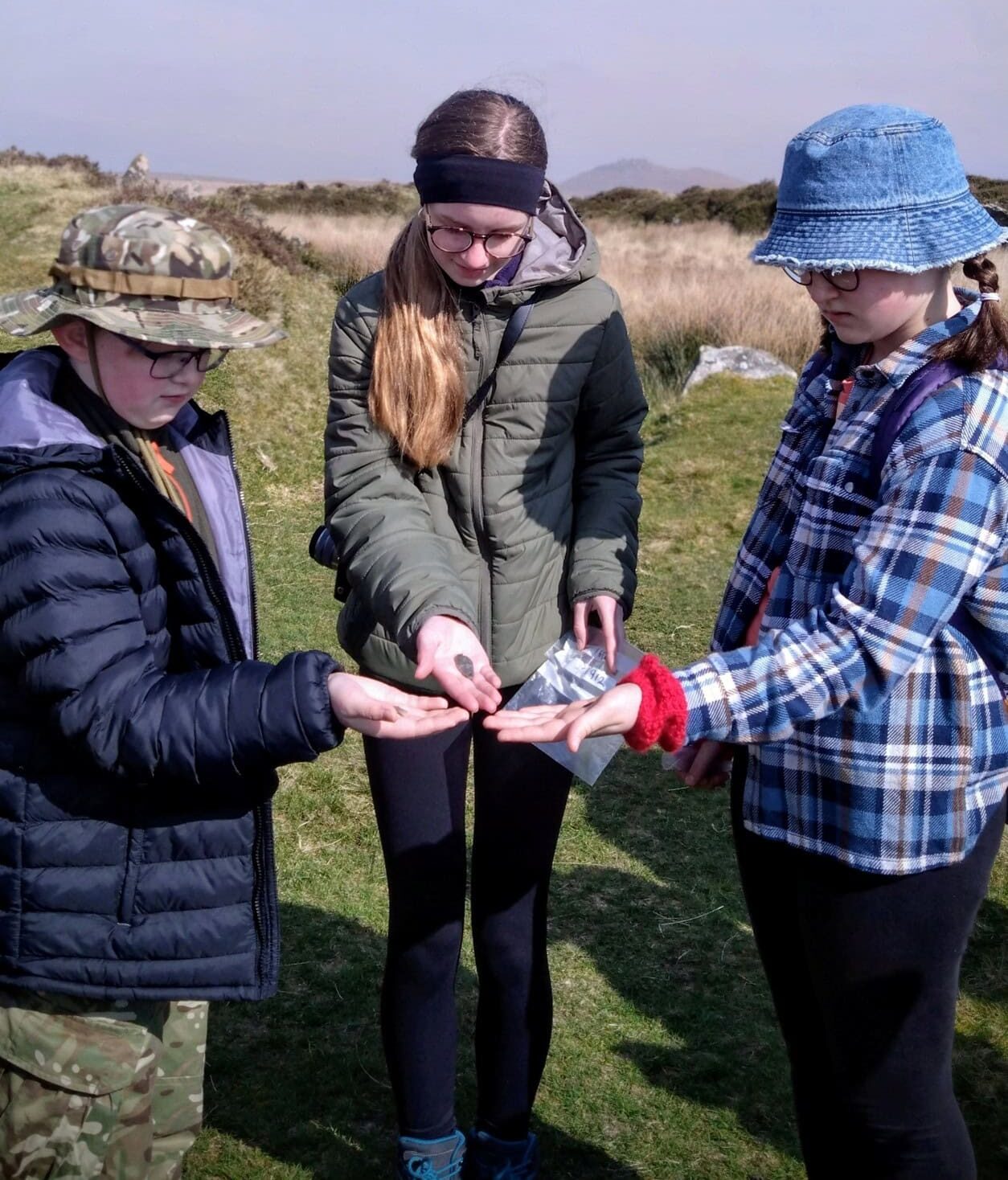 Three young people examining small hand-held artefacts in a field.