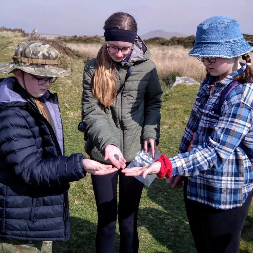 Three young people examining small hand-held artefacts in a field.
