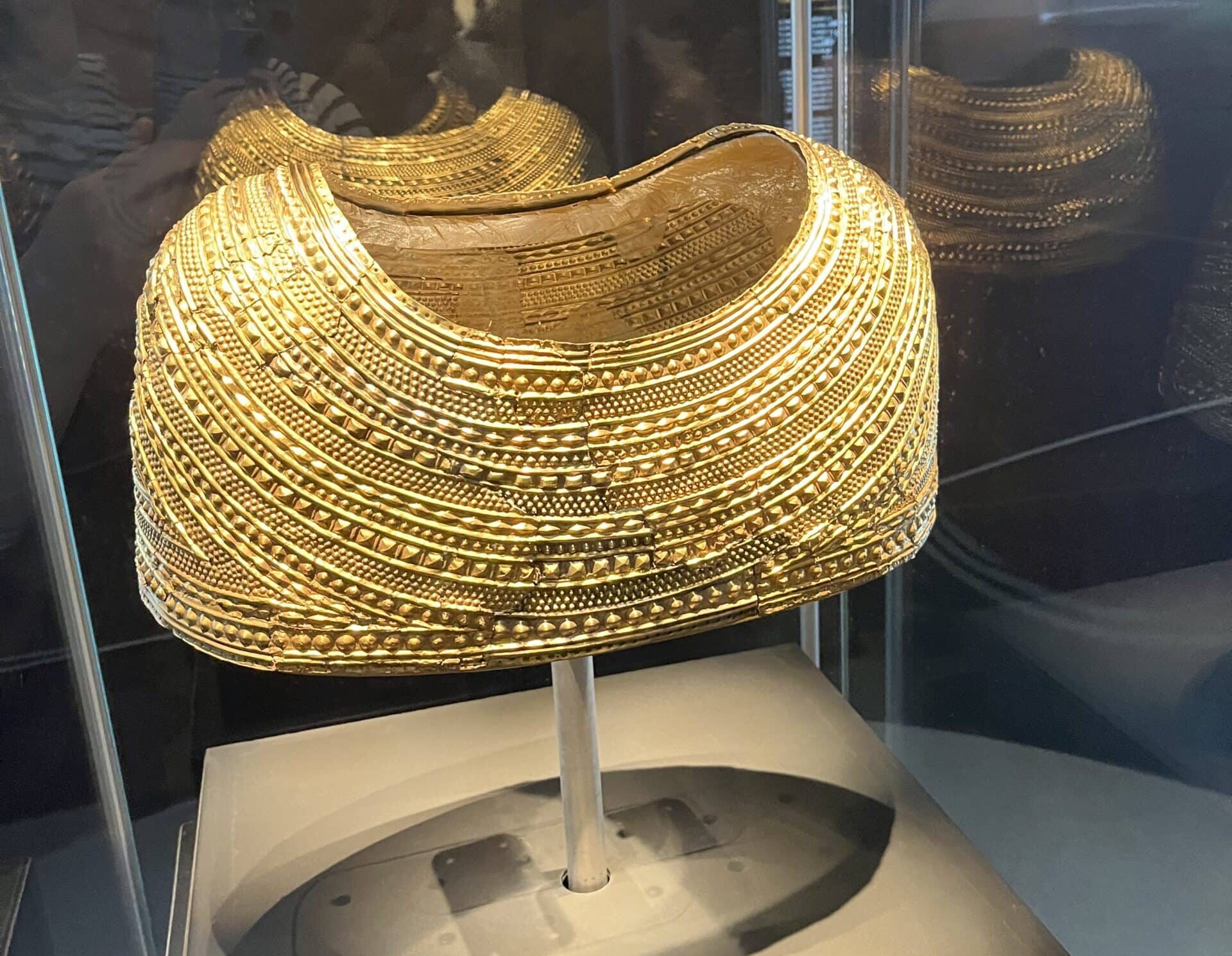 A narrow cape made from solid gold, patterned like strings of beads.
