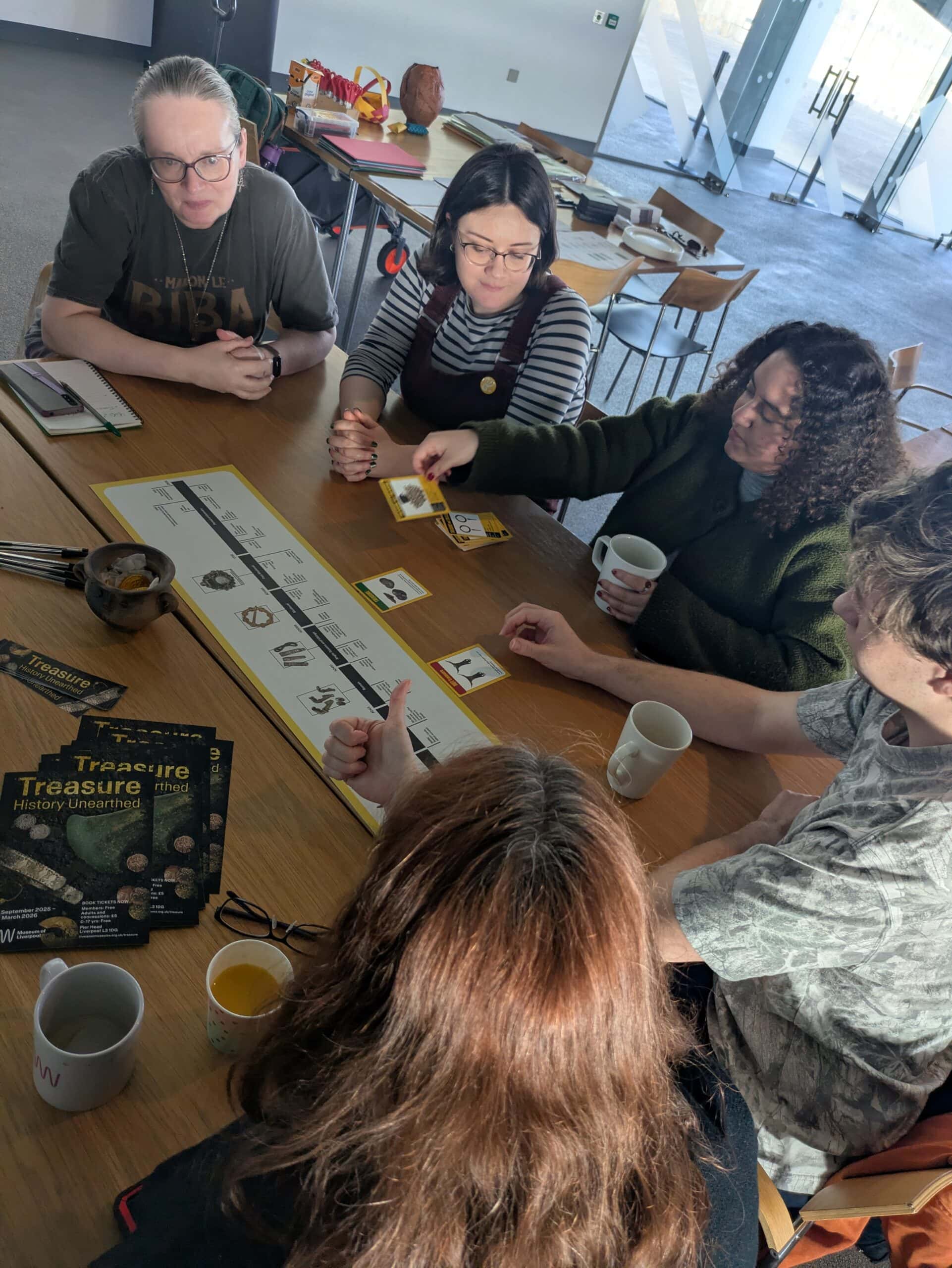 A group of adults sat around a table looking at small printed cards with pictures of artefacts on them