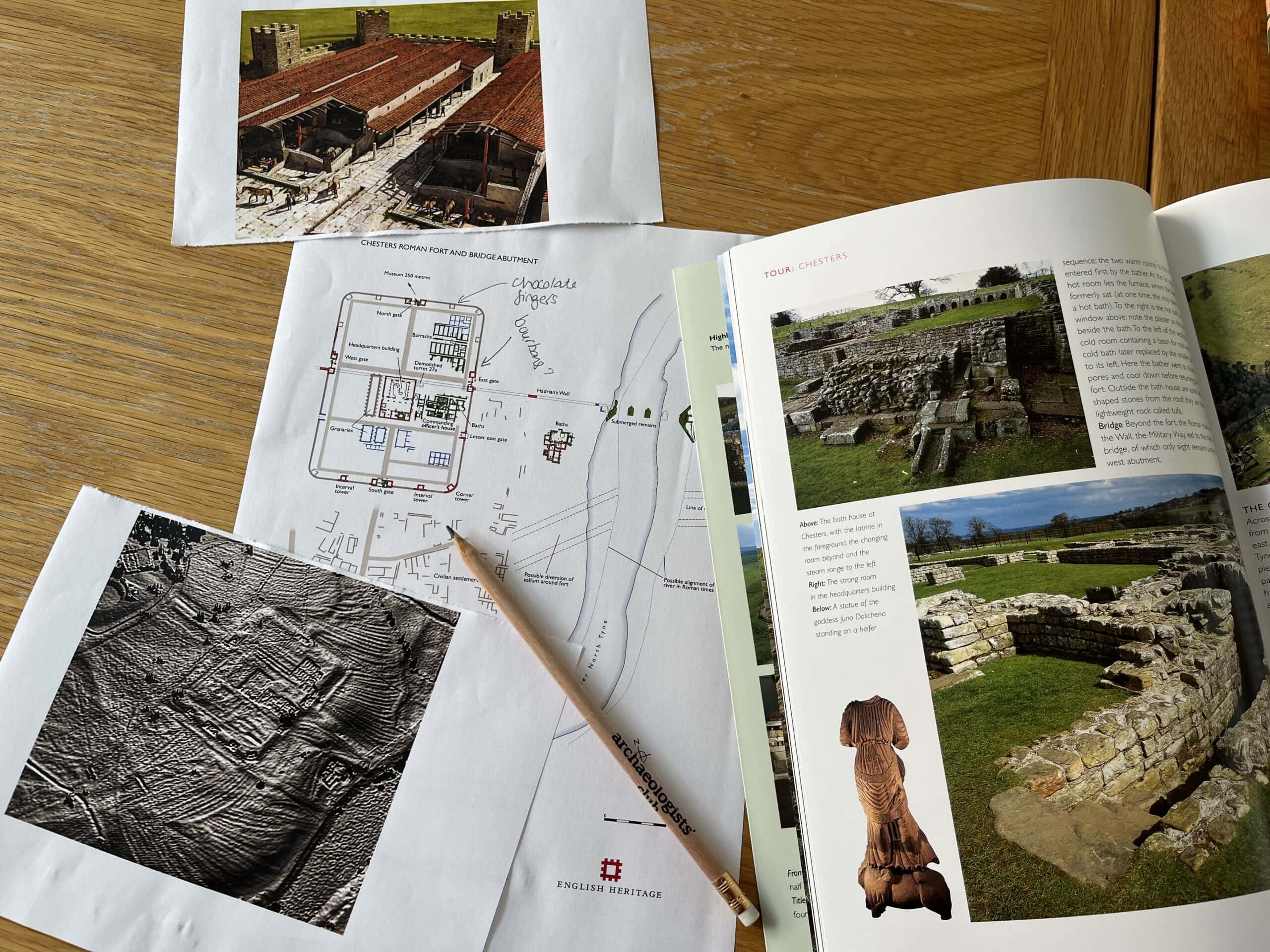 A selection of drawings and images of an archaeological Roman fort laid on a wooden table with a pencil