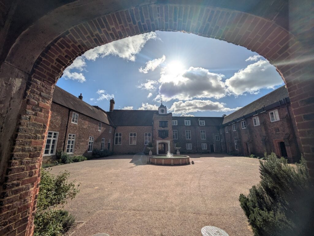 Photo of internal courtyard with brick and stone building. Fountain in the centre