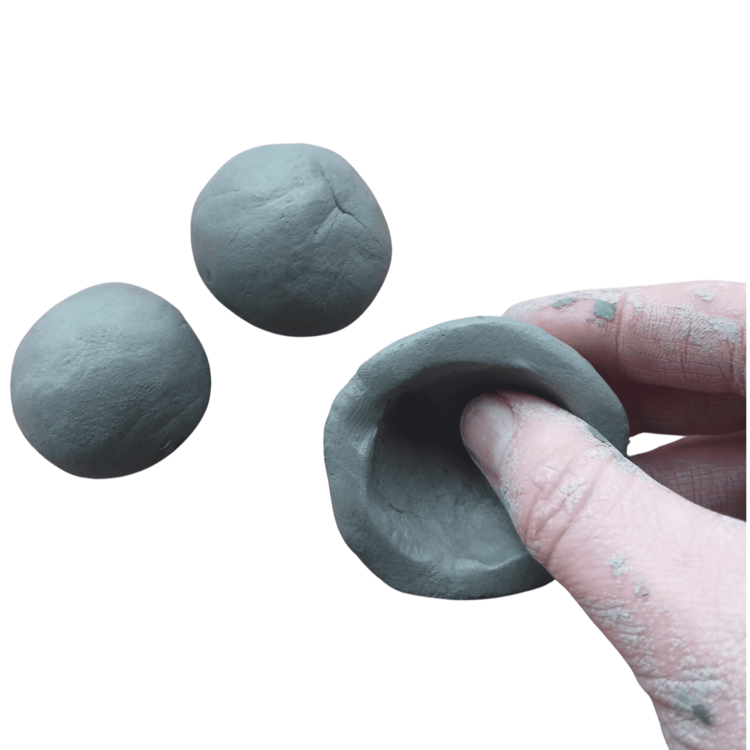 Two small balls of clay. A third piece of clay is being pinched into a small bowl with a person's fingers.