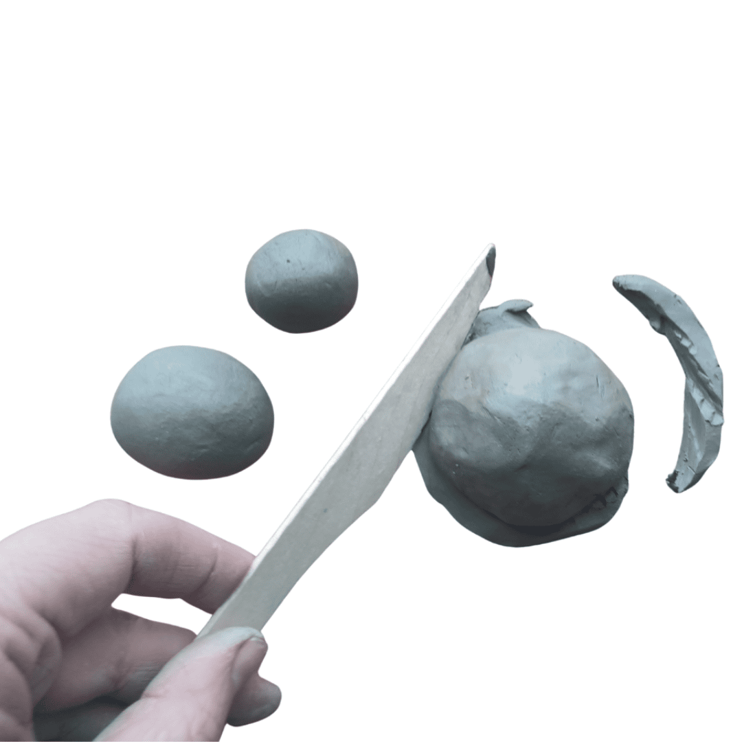 Three small balls of clay, one of which is being trimmed with a wooden knife.